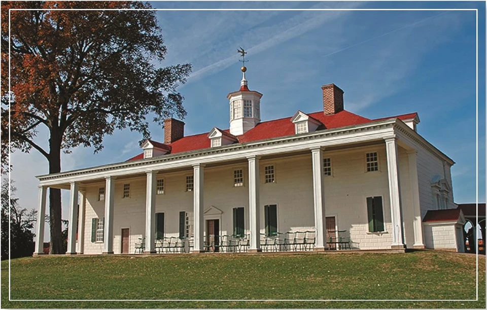 A historic building with columns and a red roof surrounded by greenery